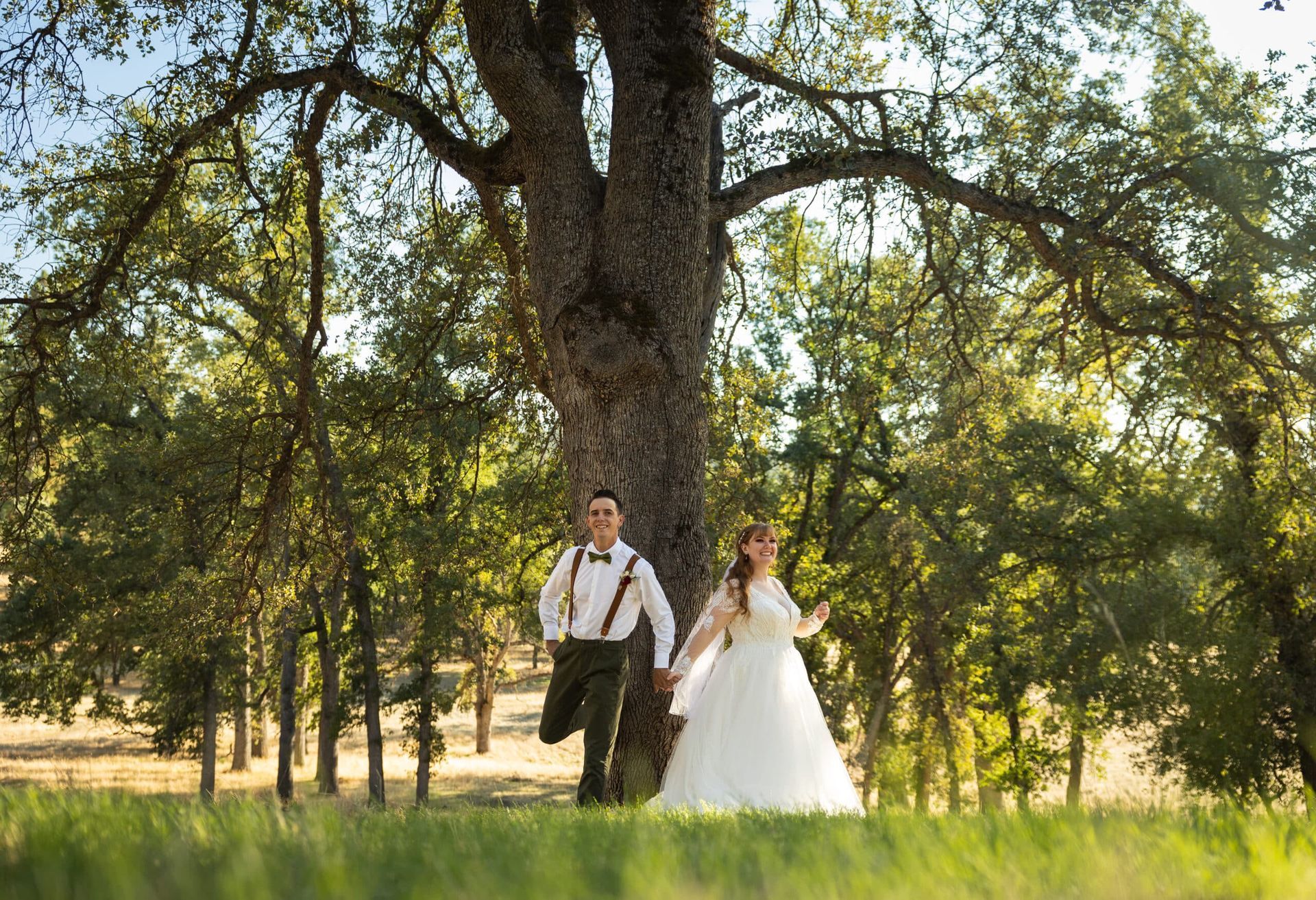 A bride and groom are holding hands in front of a large tree.