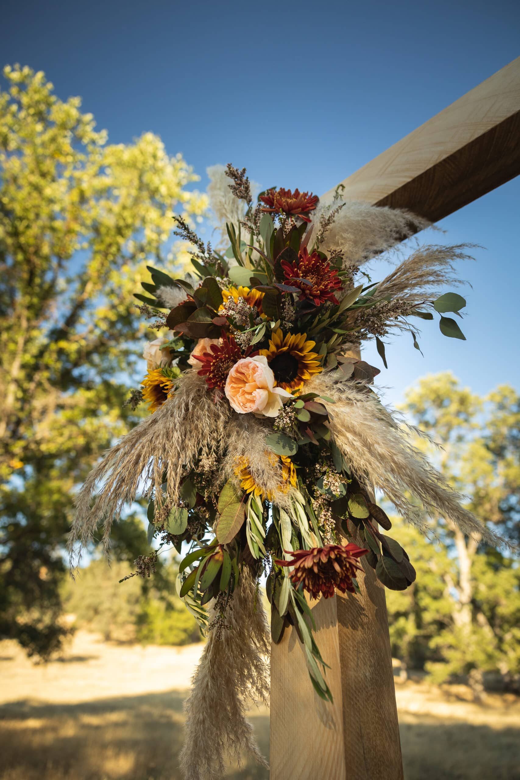 A wooden arch decorated with flowers and pampas grass for a wedding ceremony.