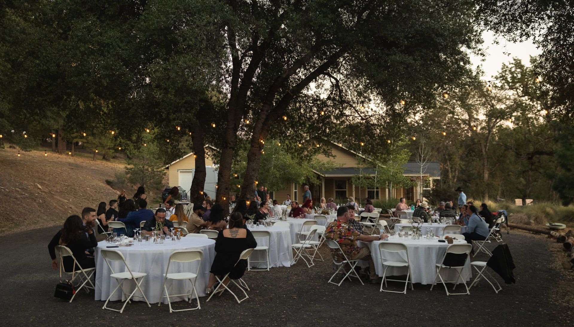 A group of people are sitting at tables outside in front of a house