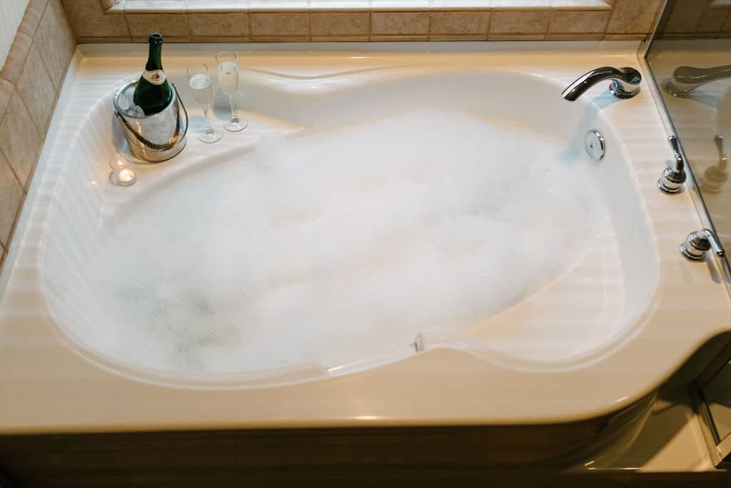 A bathtub filled with bubbles and a bottle of champagne.