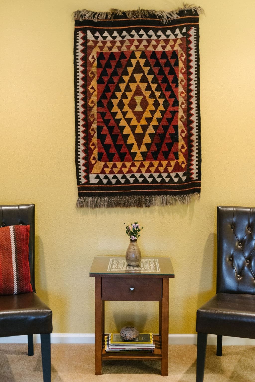 A room with two chairs and a rug on the wall