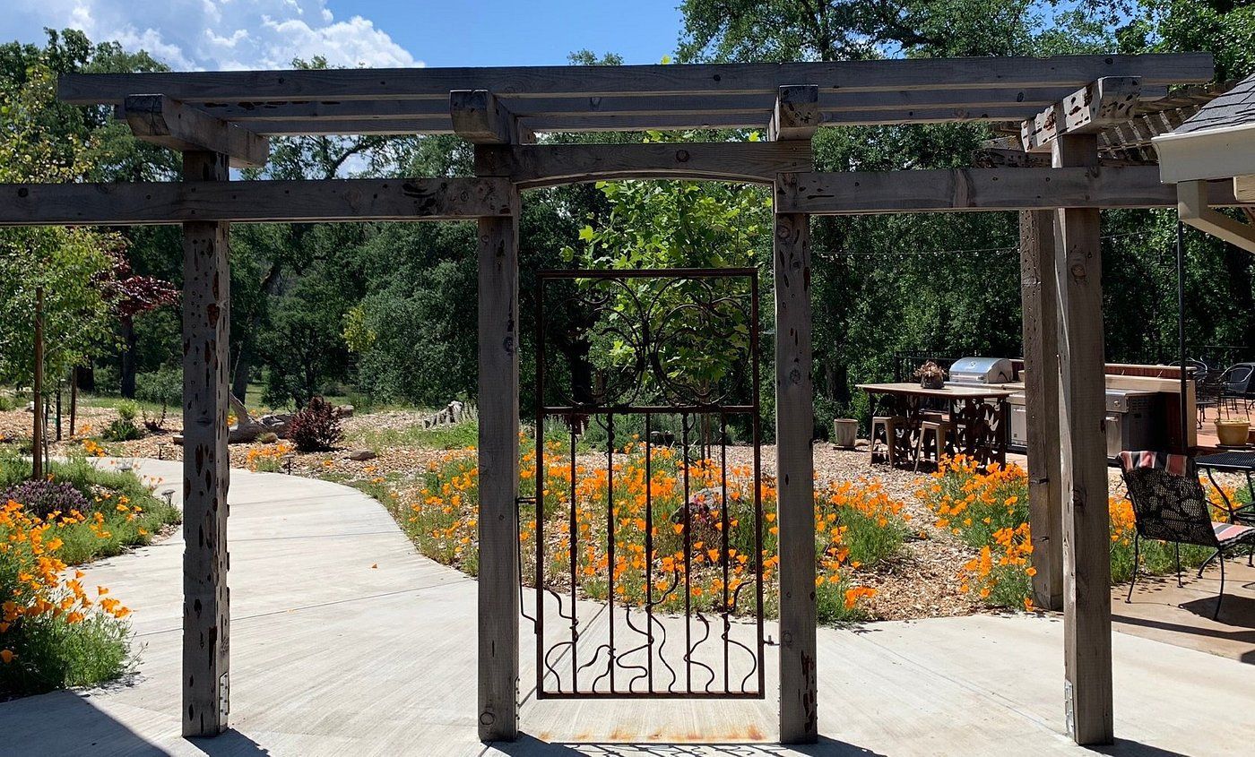 A wooden pergola with a gate in the middle of a garden.