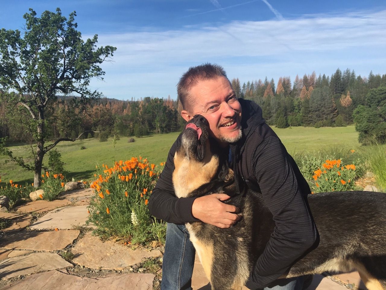 A man is hugging a german shepherd dog in a field.