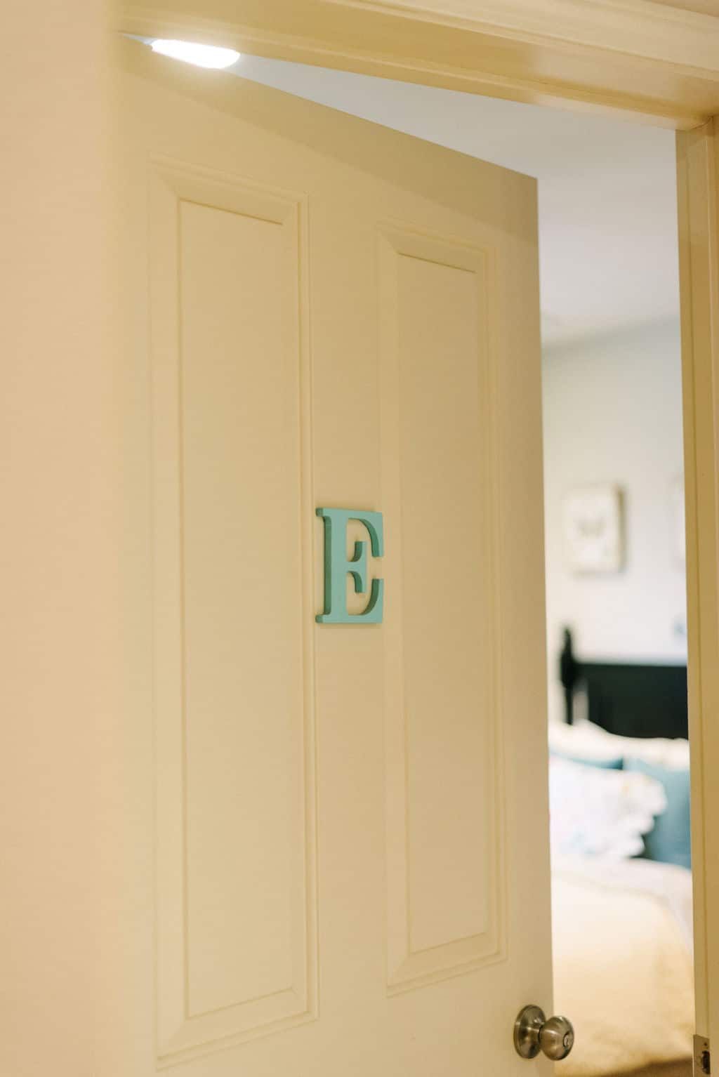 A white door with a blue letter e on it is open to a bedroom.