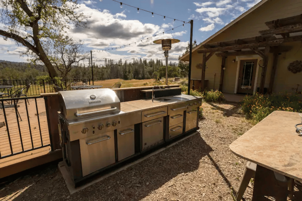 An outdoor kitchen with a grill and a table in front of a house.