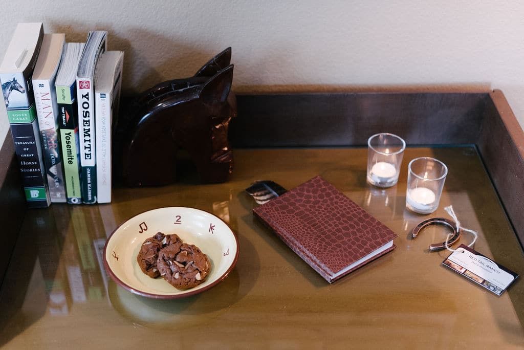 A table with a bowl of cookies , a notebook , candles , and books.