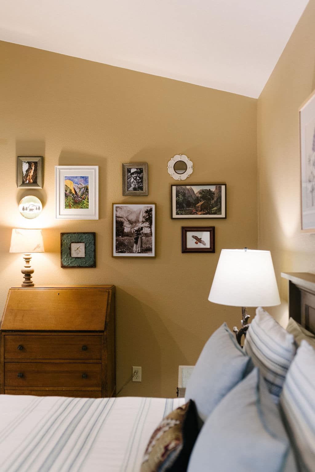 A bedroom with a bed , dresser , lamp and pictures on the wall.