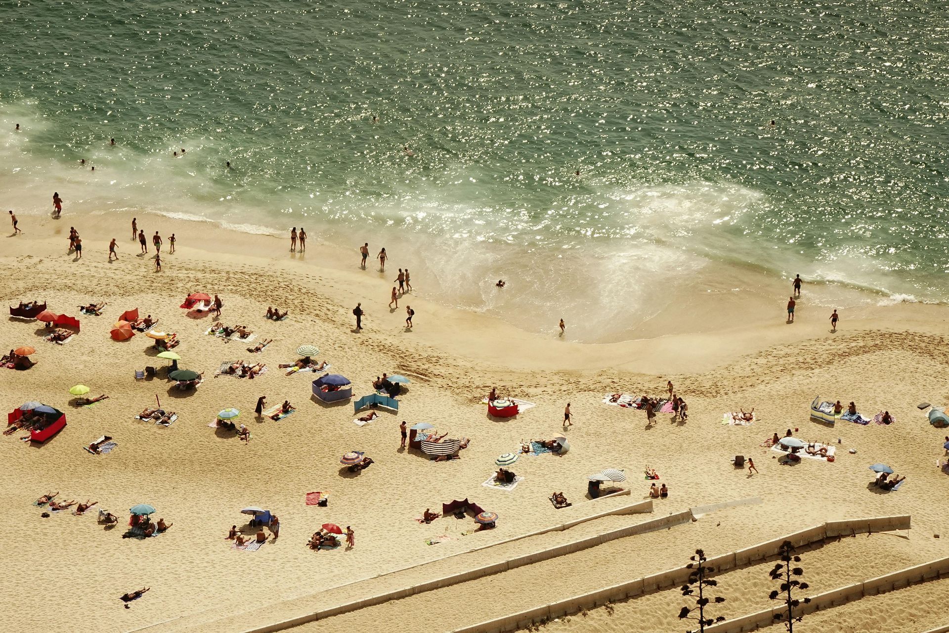 Beach scene with many people, colorful umbrellas, and sparkling ocean.