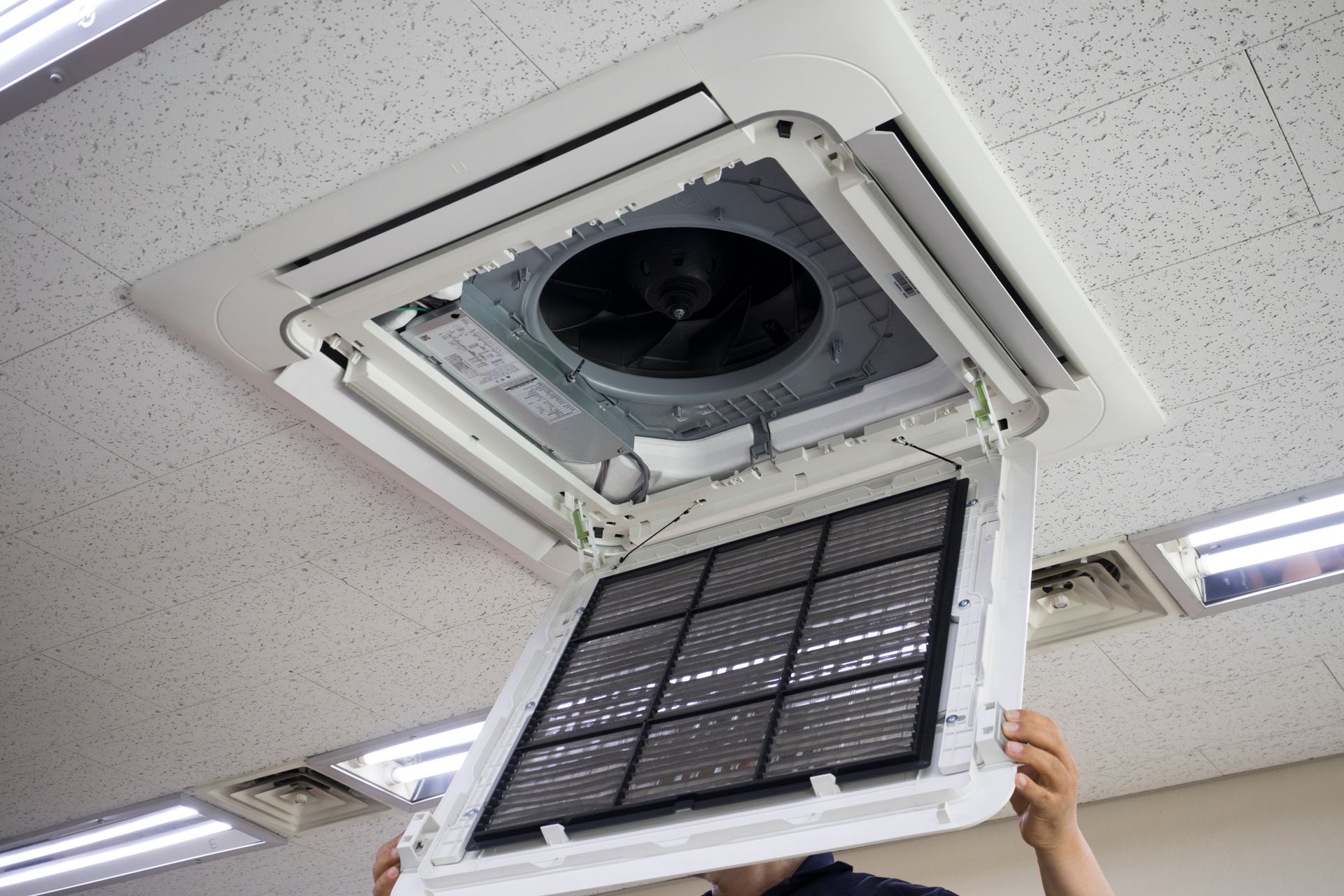 Open ceiling HVAC unit with a person holding a removed air filter panel.