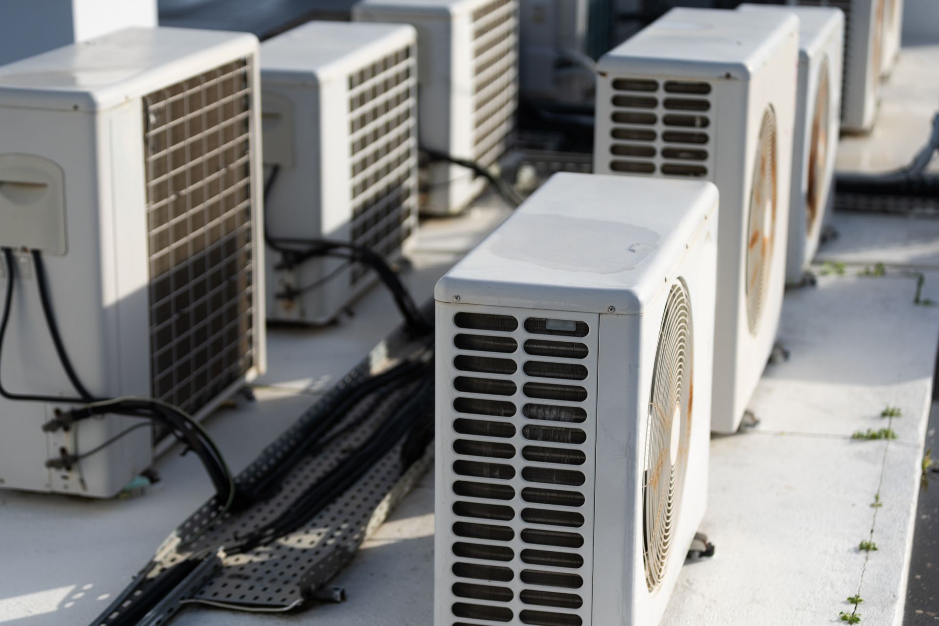 Row of outdoor air conditioning units with black cables on a rooftop or industrial surface