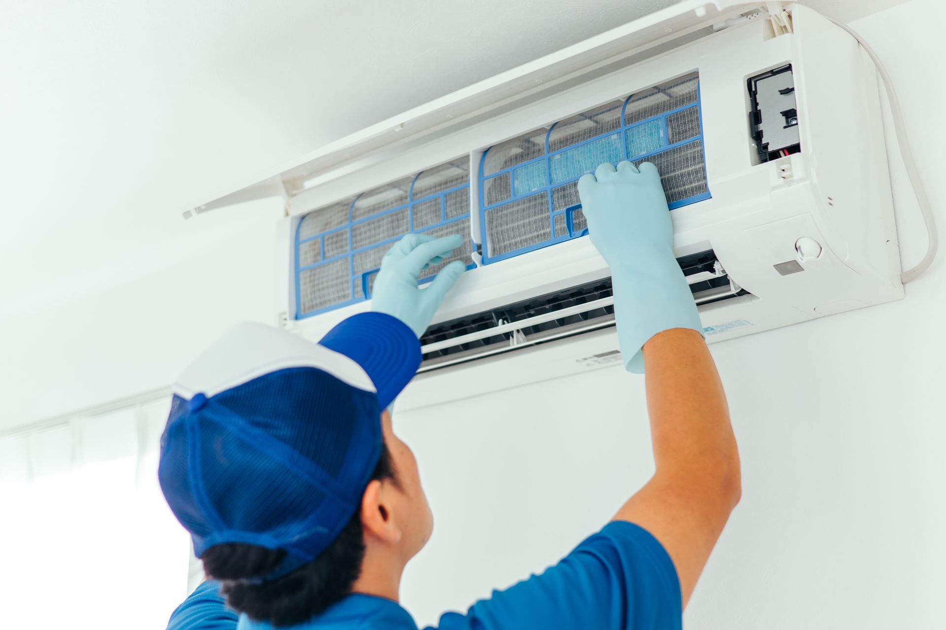 Technician cleaning an air conditioner filter with gloves and tools in a white room