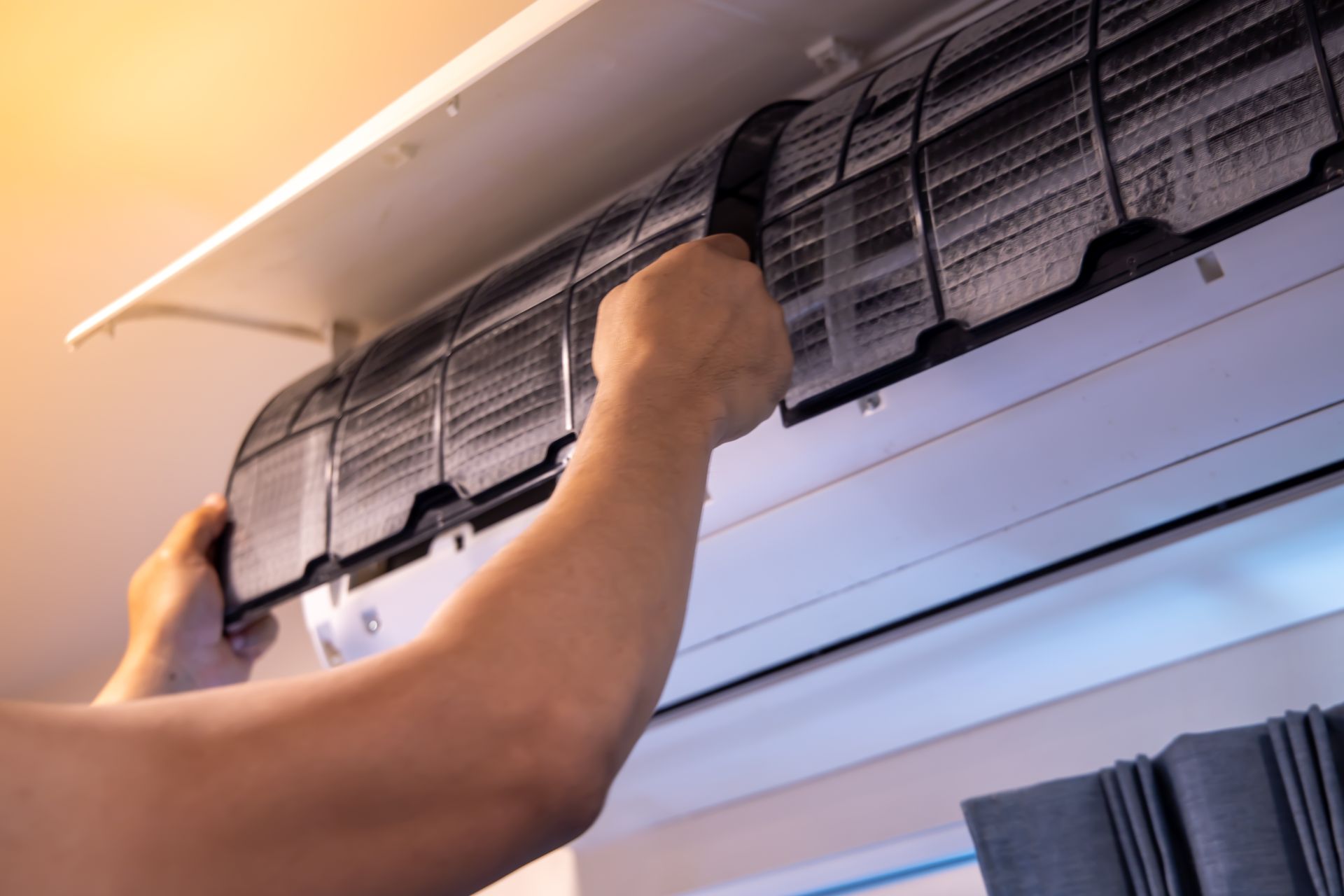 Person cleaning a wall-mounted air conditioner filter with hands