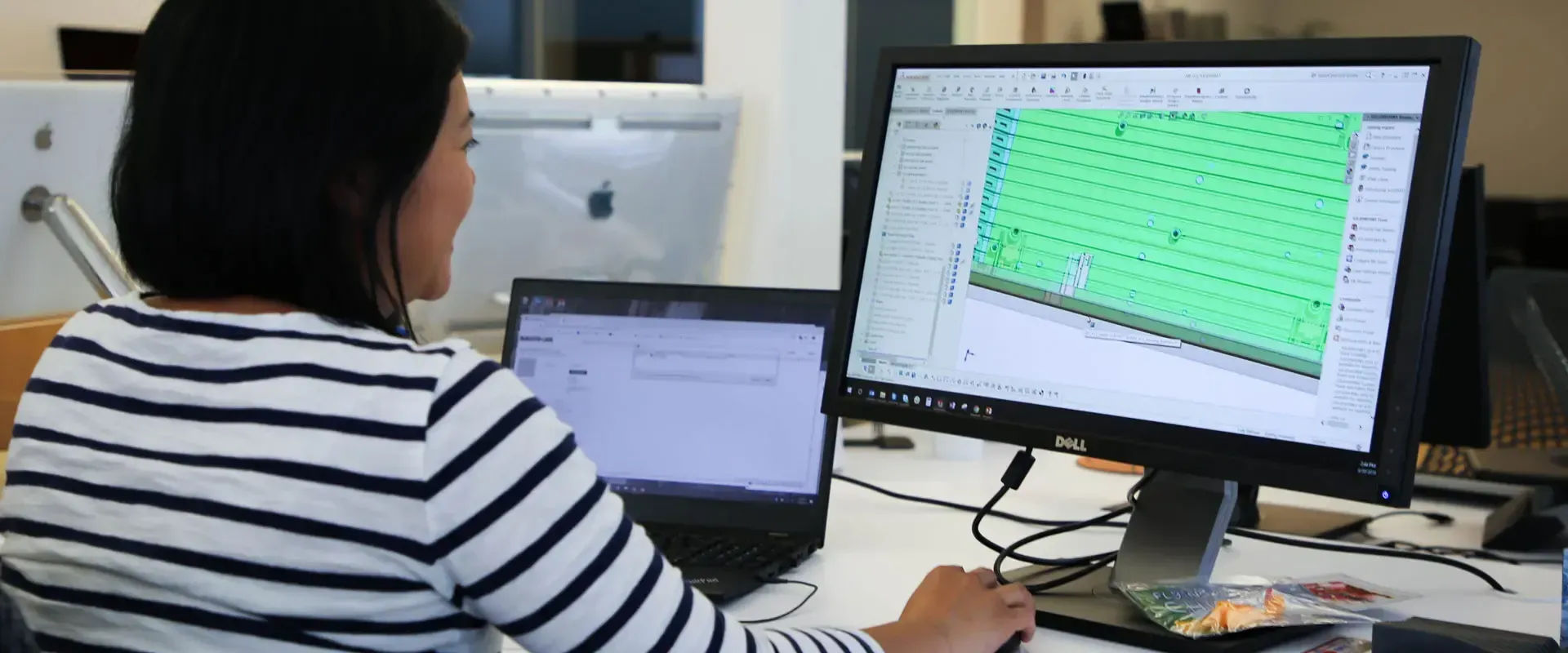 Woman working at a computer, looking at a green-filled screen. She wears a striped shirt.