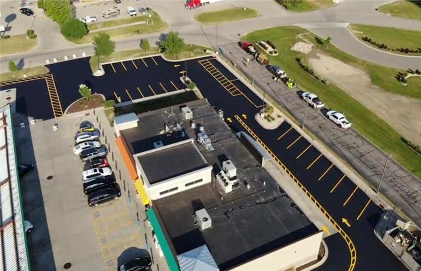 Aerial view of a newly paved parking lot with yellow parking lines, cars, and a building.