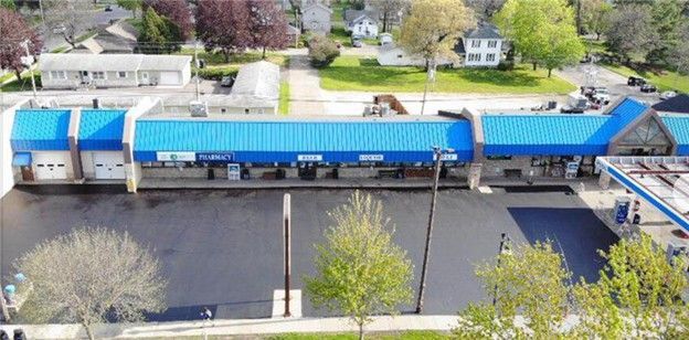 An aerial view of a car wash with a blue roof and gas station, trees in the foreground.