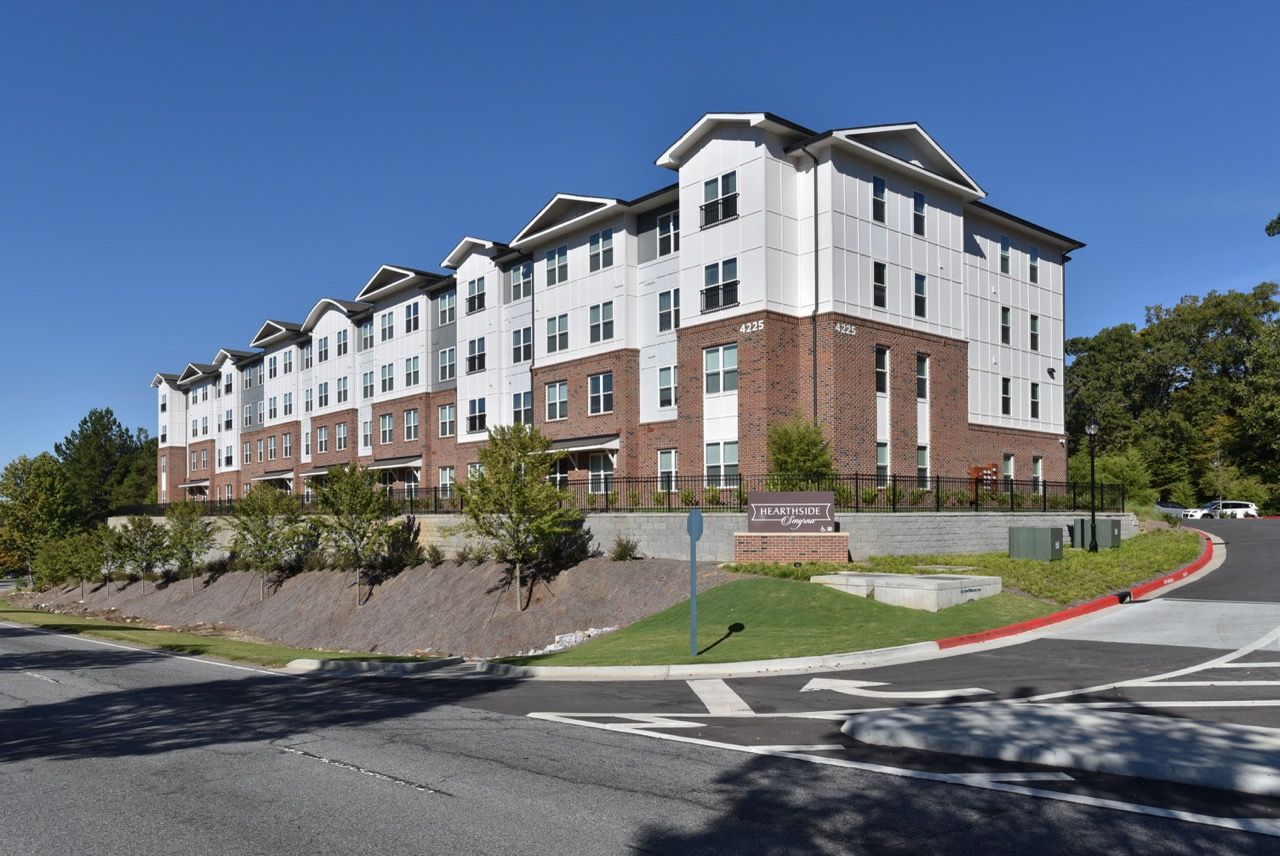 Exterior view of a modern multi-story apartment building with brick base, light siding, and landscaped grounds.