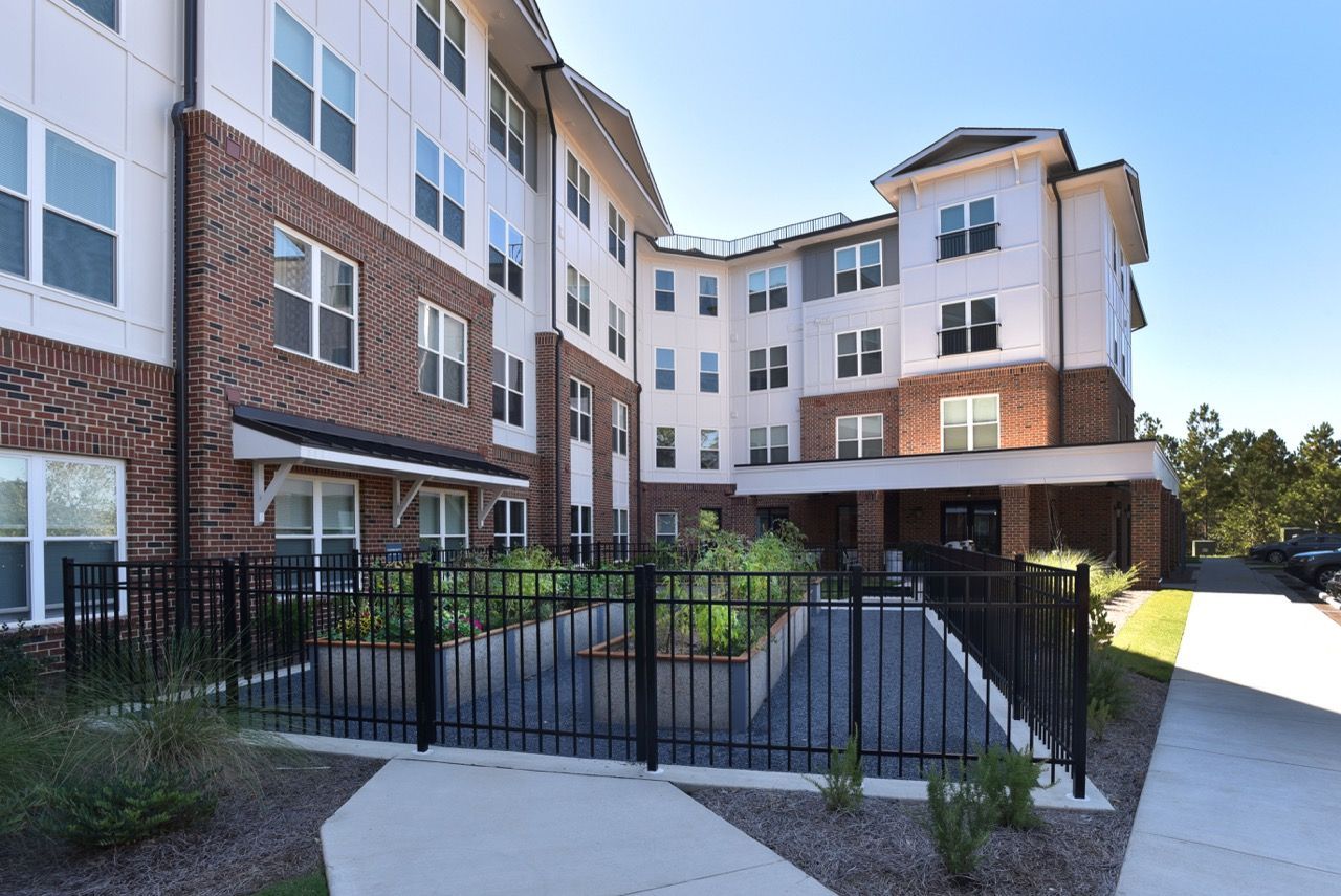 Exterior view of a multi-story apartment building with brick lower level, white siding, and a fenced central courtyard.