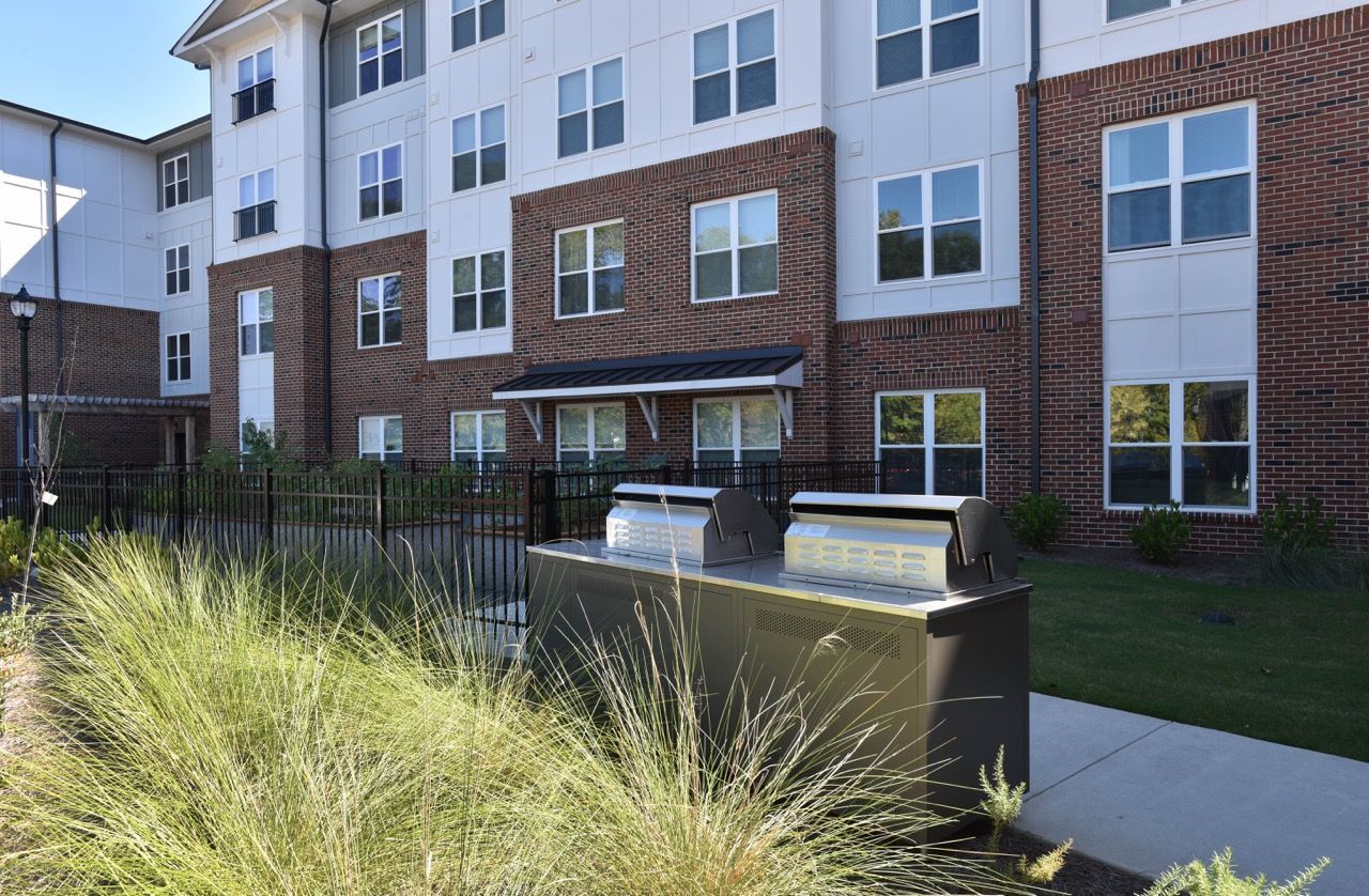 Exterior view of a multi-story apartment building with brick and white siding and a communal grilling area.