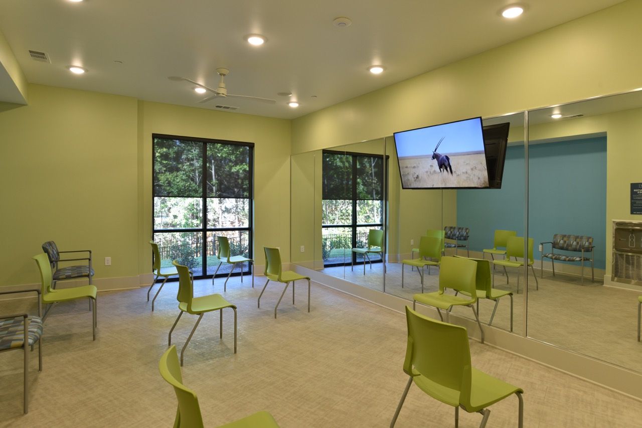 Interior of a community lounge with lime-green chairs, large mirrors, and a wall-mounted TV.