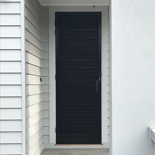 A black standard steel security door is sitting on a white wall next to a white wall.