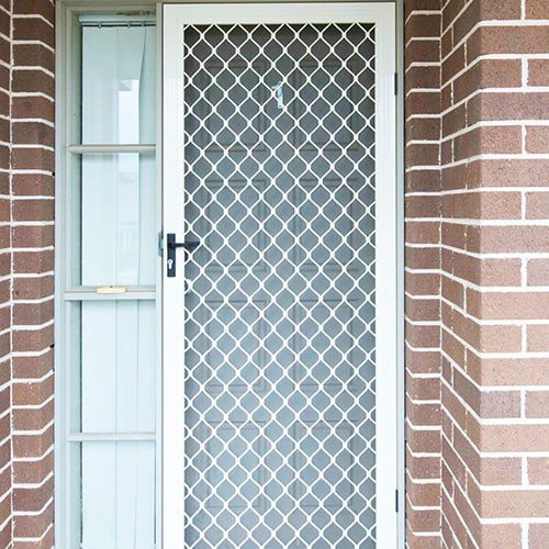 A home white door with a diamond security pattern on it is on a brick wall.