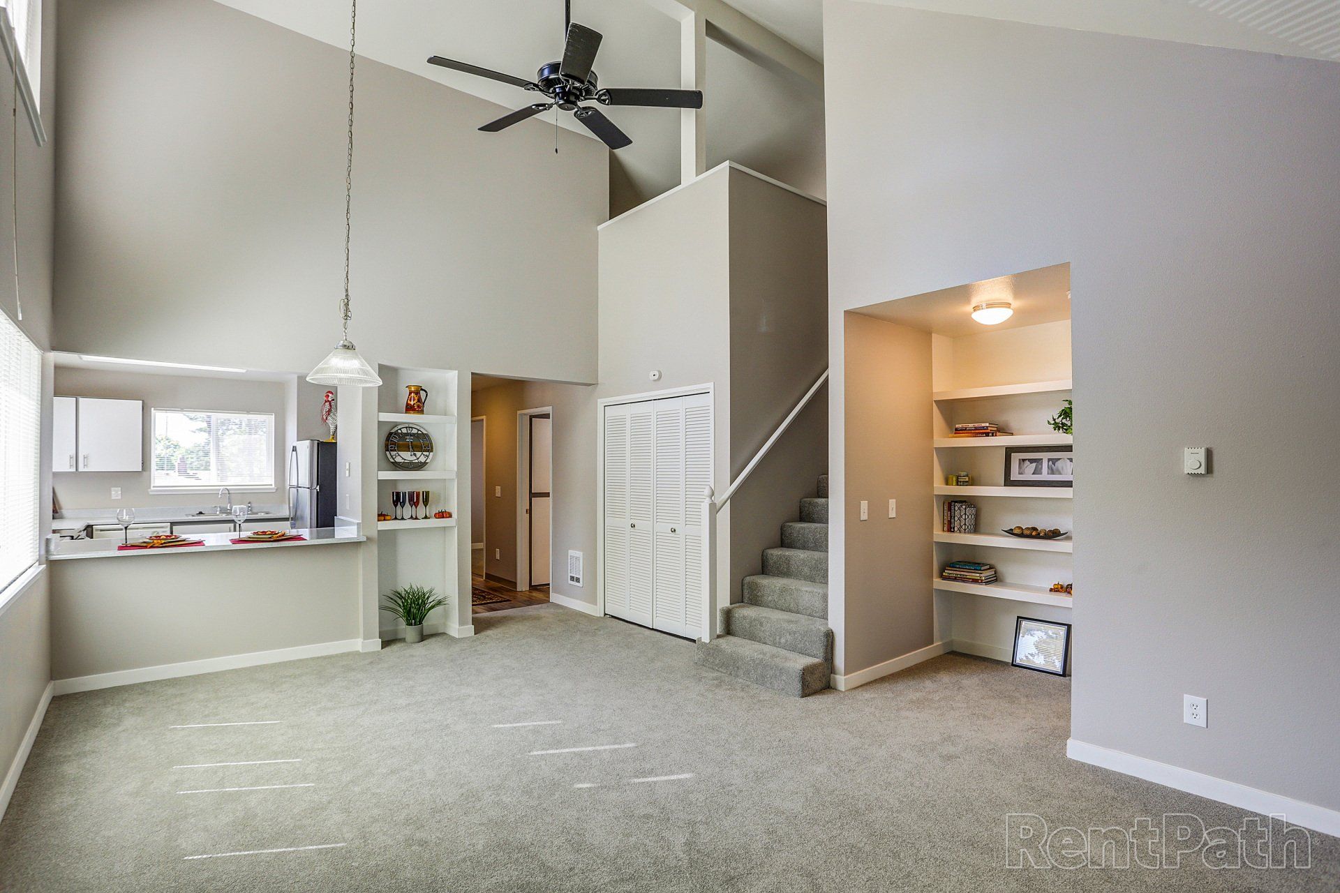 A living room with a ceiling fan and stairs leading up to the second floor.