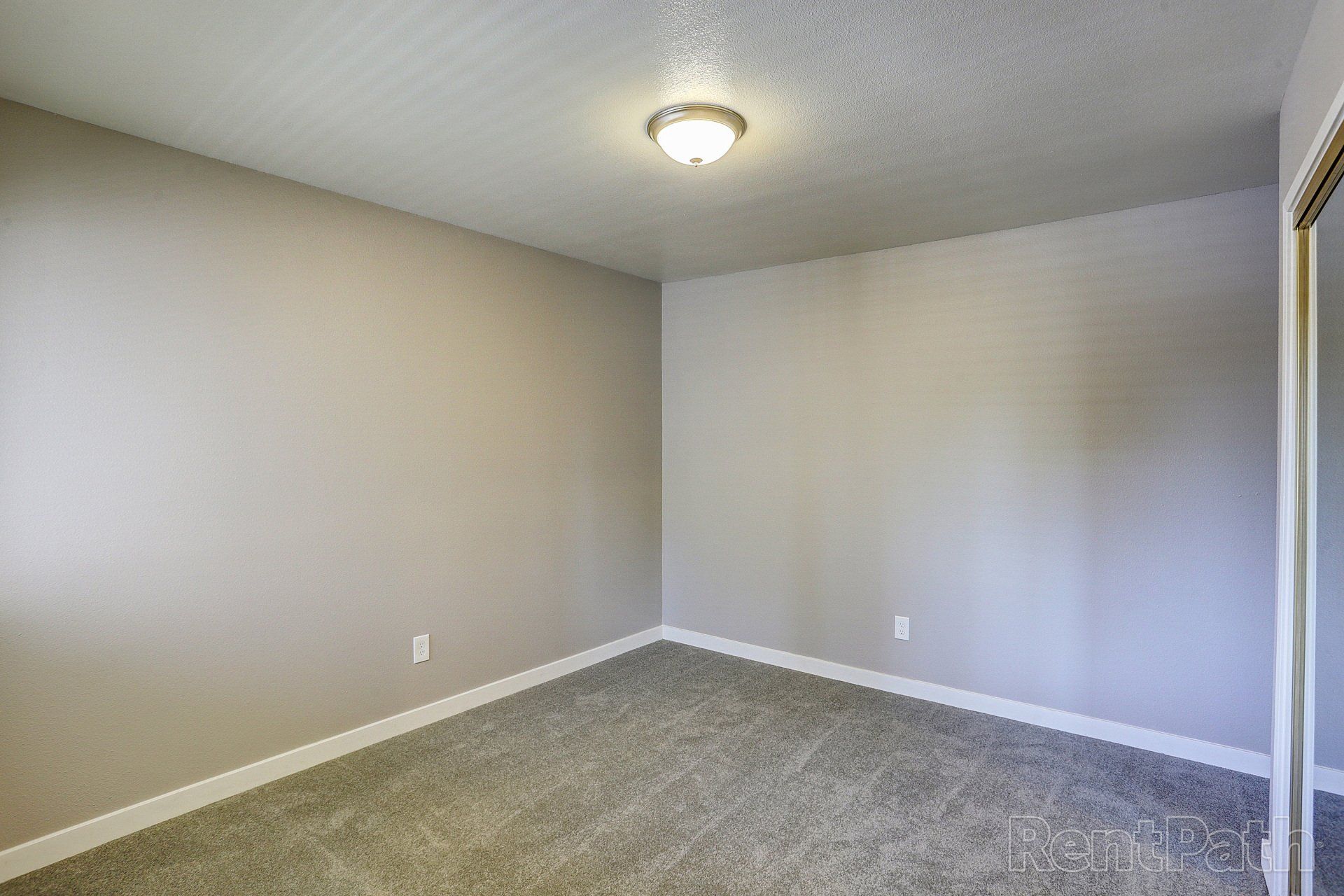An empty bedroom with a carpeted floor and a light fixture on the ceiling.