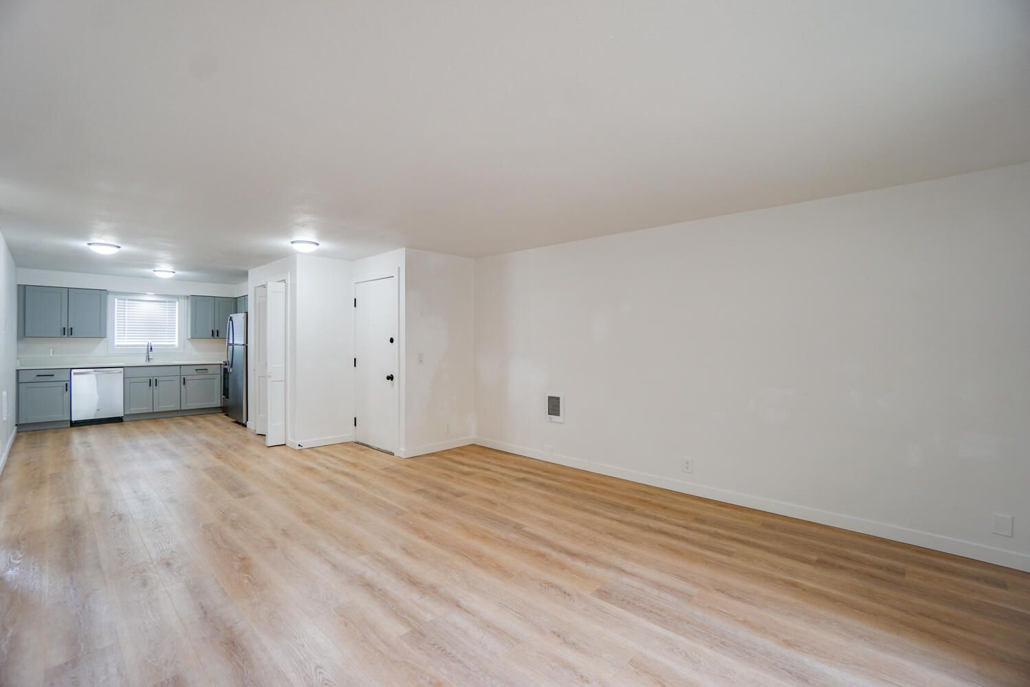 An empty living room with hardwood floors and a kitchen in the background.