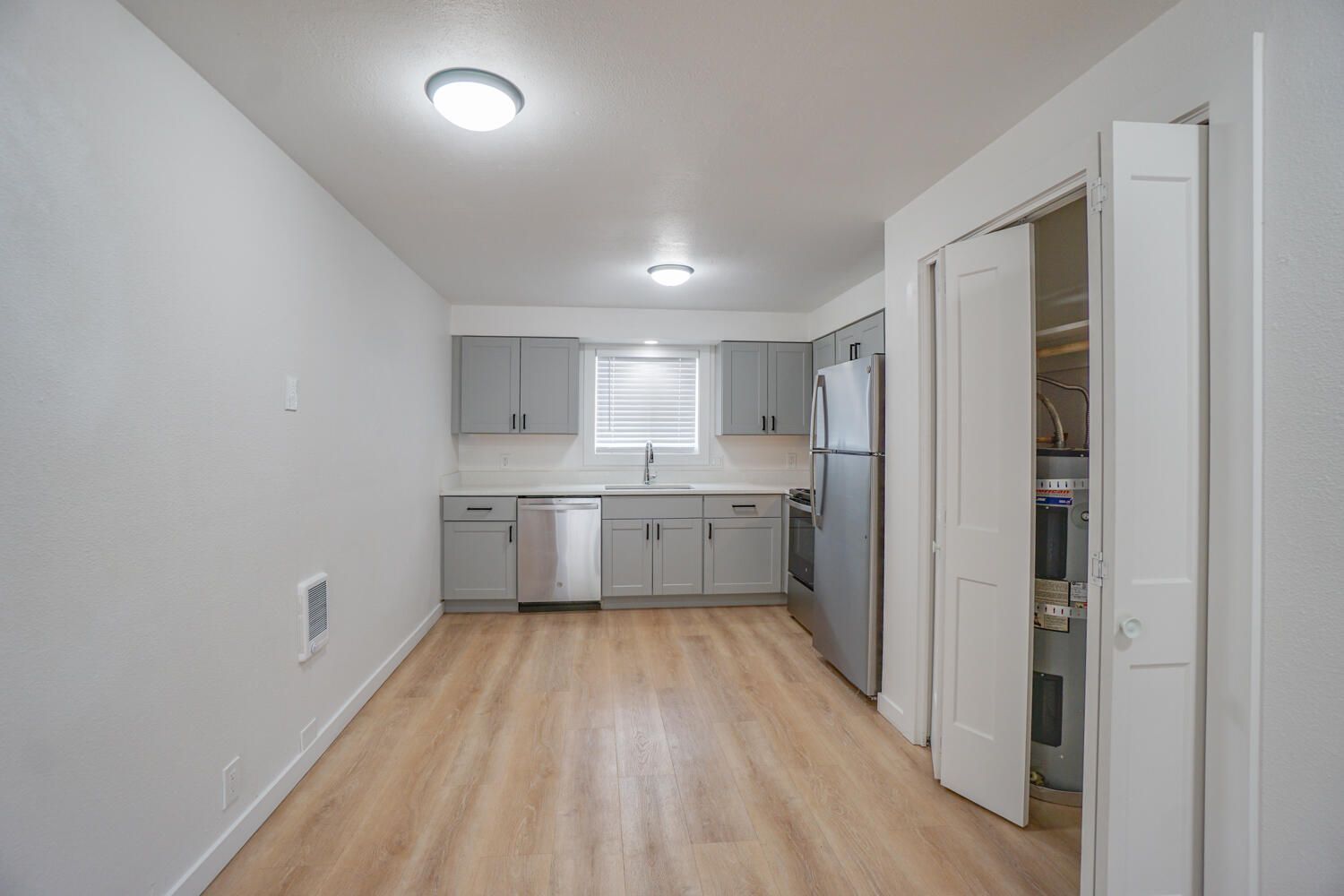 An empty kitchen with stainless steel appliances and wooden floors.