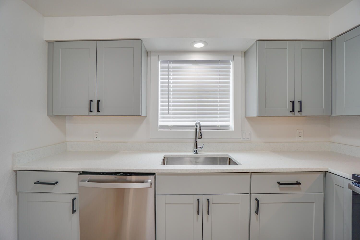 A kitchen with white cabinets , stainless steel appliances , a sink and a window.