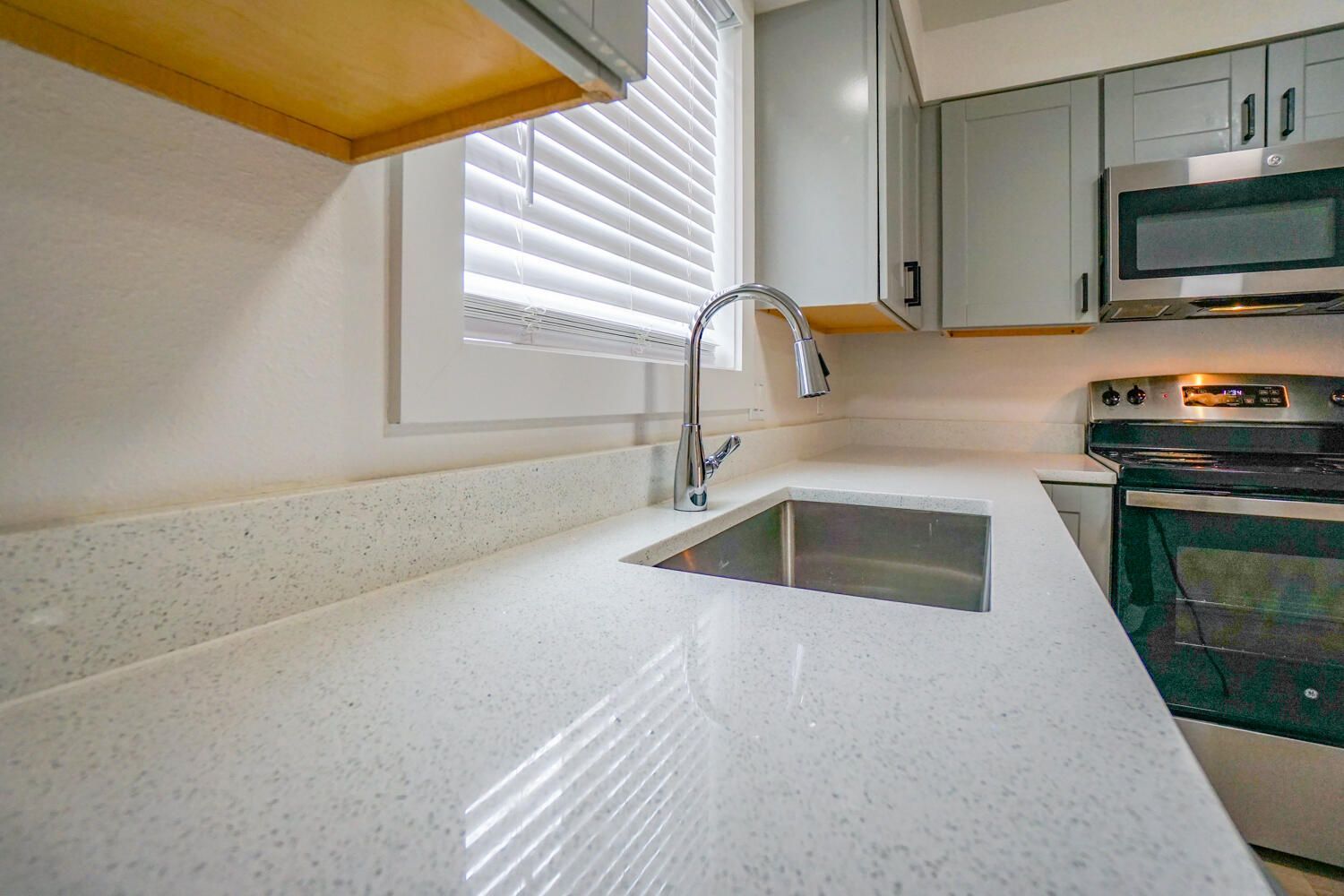 A kitchen with a sink , stove , microwave and window.