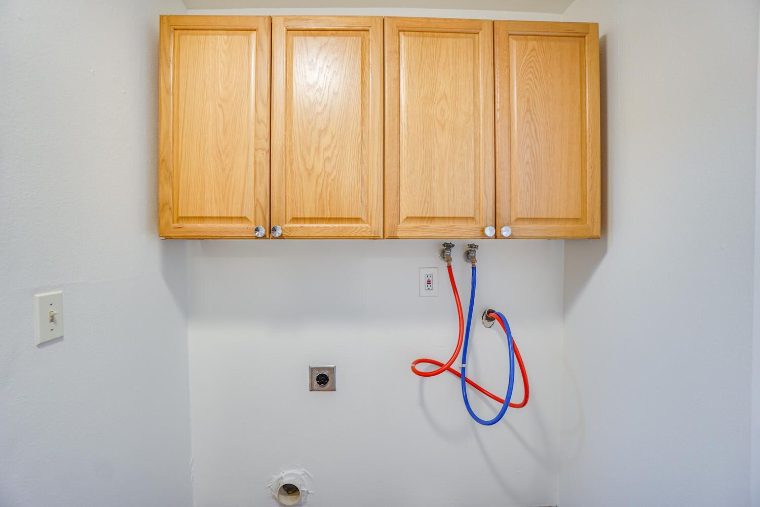 A laundry room with wooden cabinets and red and blue hoses hanging from the wall.