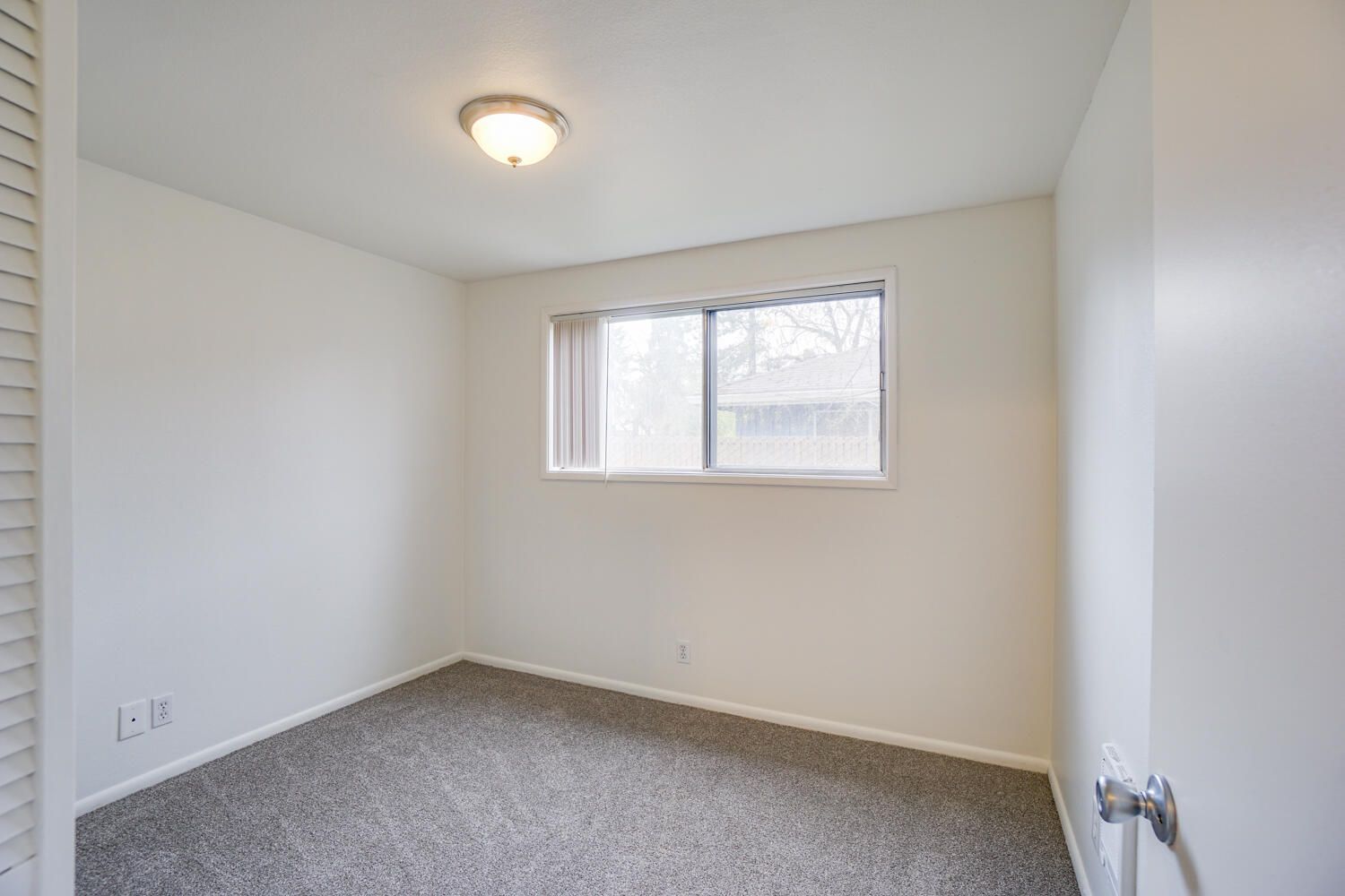 An empty bedroom with a window and a sliding glass door.