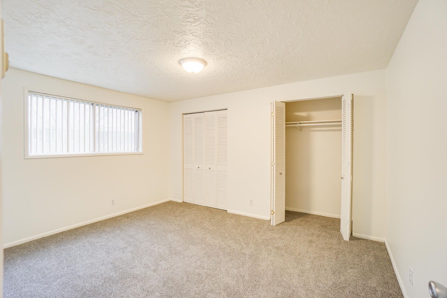 An empty bedroom with a closet and a window.