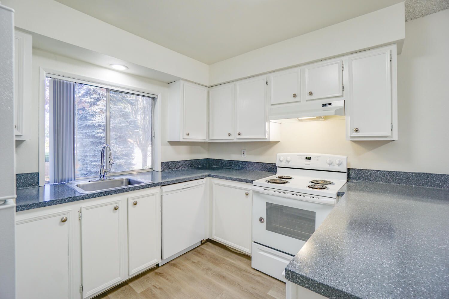 A kitchen with white cabinets , a stove , a sink , and a window.