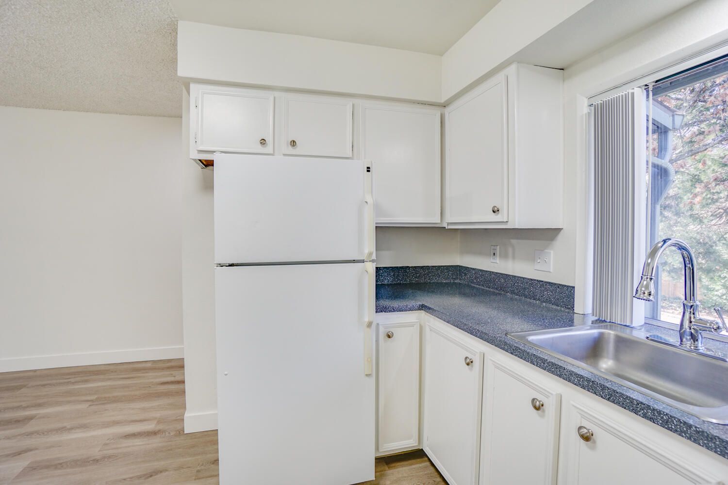 A kitchen with white cabinets , a refrigerator , a sink and a window.