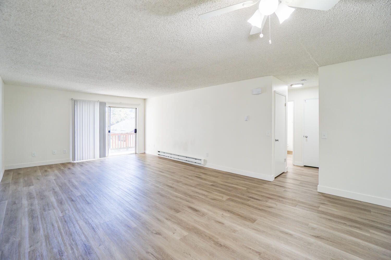 An empty living room with hardwood floors and a ceiling fan.