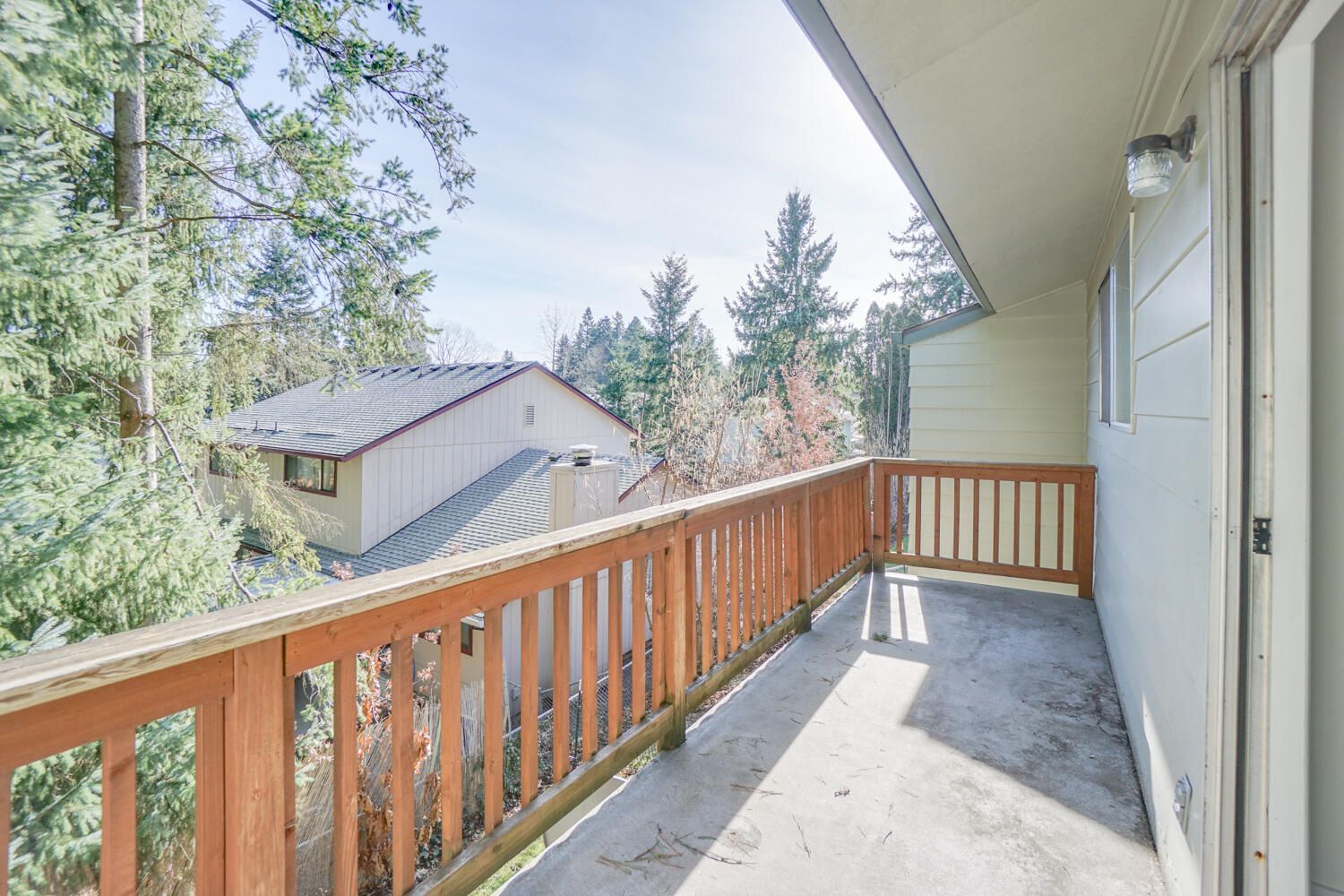 A balcony with a wooden railing and a view of a house and trees.