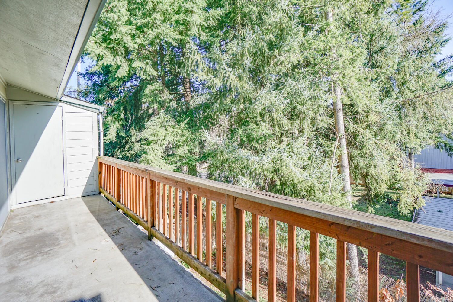 A balcony with a wooden railing and trees in the background.