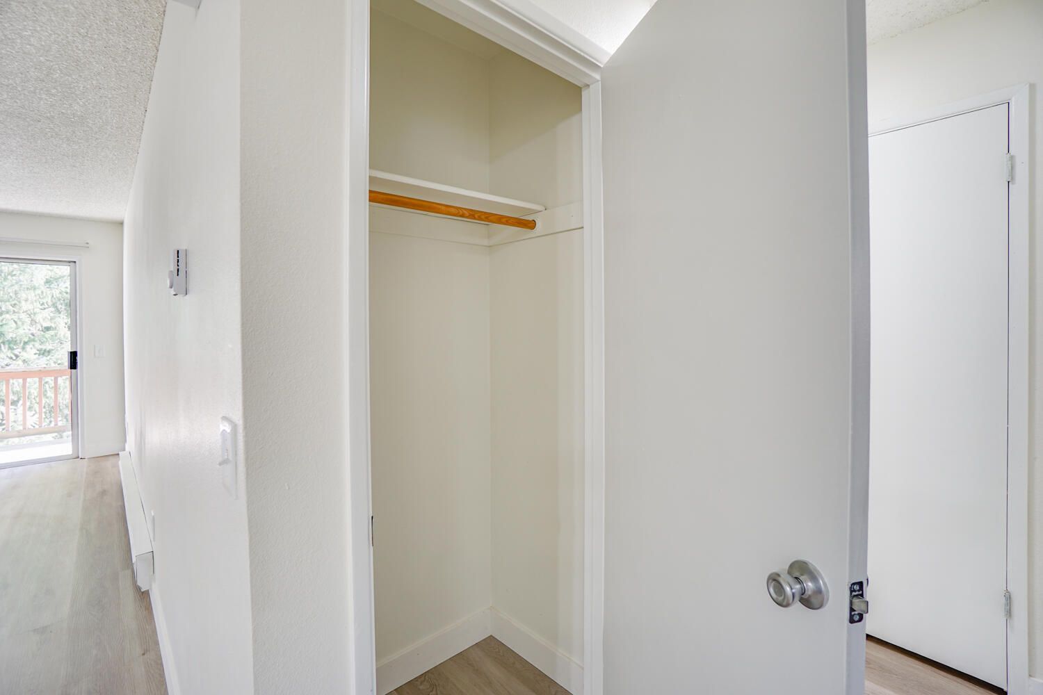 An empty closet in a hallway with a sliding glass door.