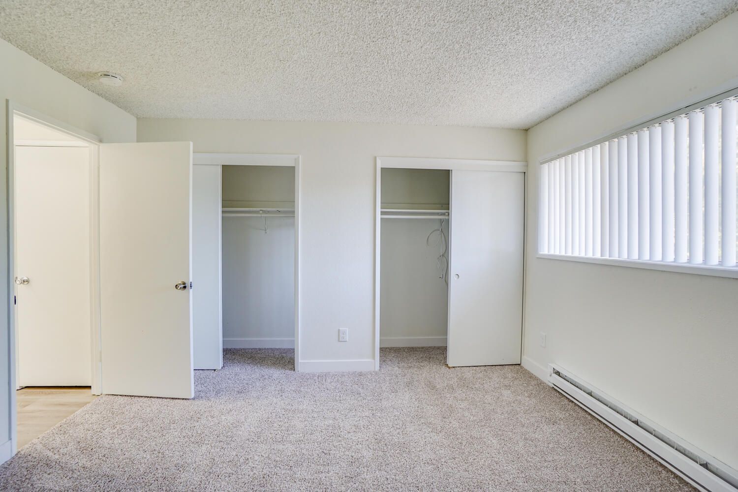 An empty bedroom with two closets and a window.