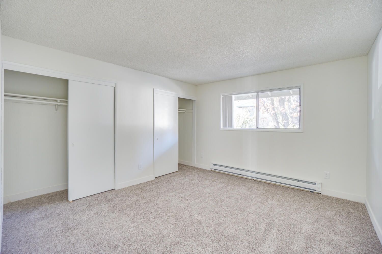 An empty bedroom with a carpeted floor , white walls , and a window.