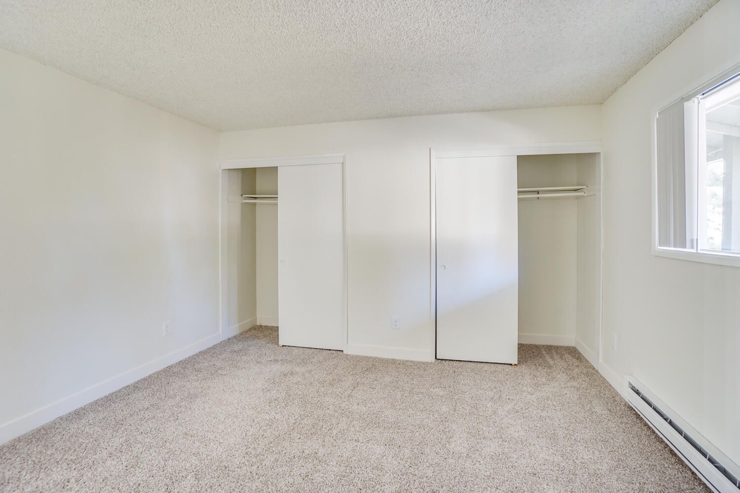 An empty bedroom with a window and closets