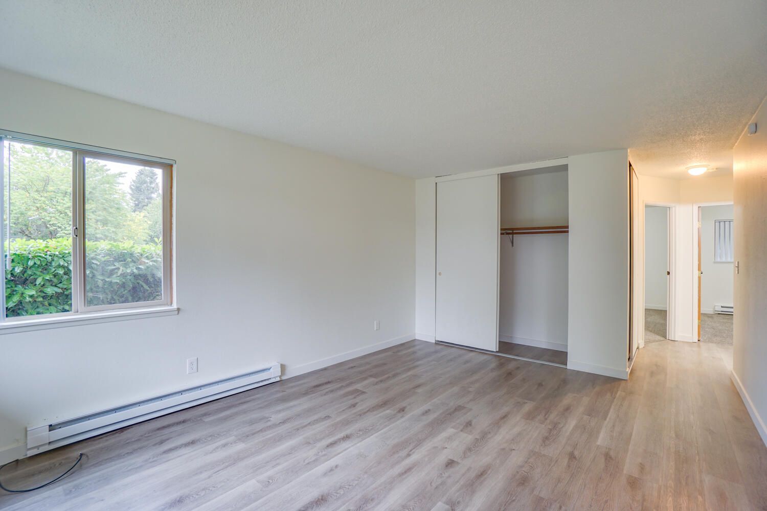 An empty living room with hardwood floors and a large window.
