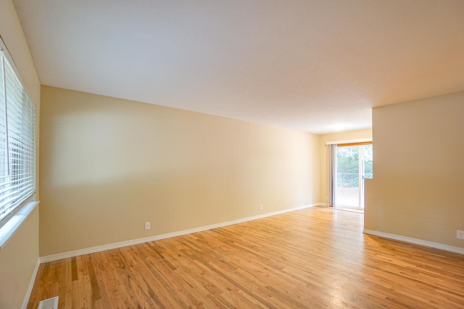 An empty living room with hardwood floors and a sliding glass door.