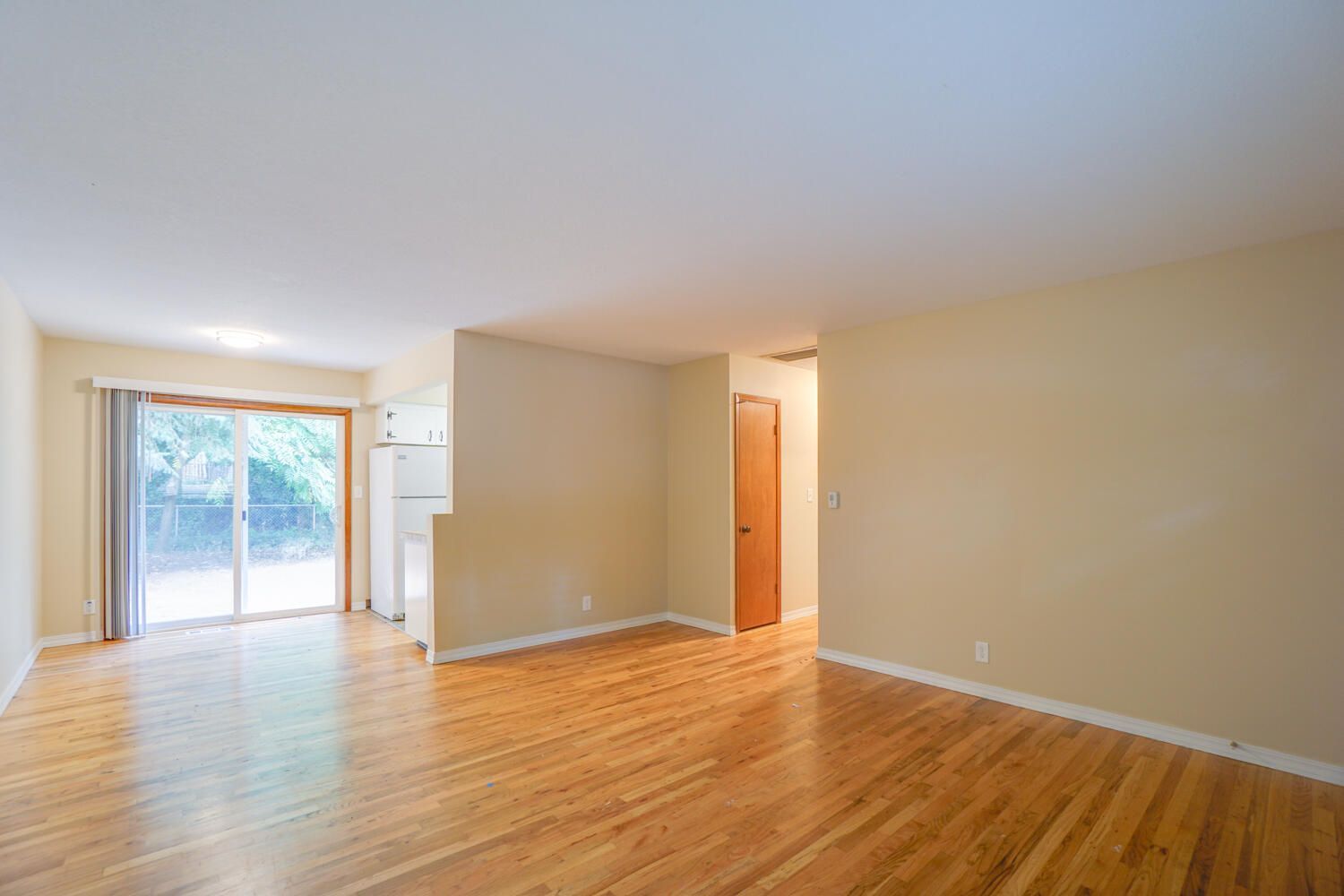 An empty living room with hardwood floors and a sliding glass door.