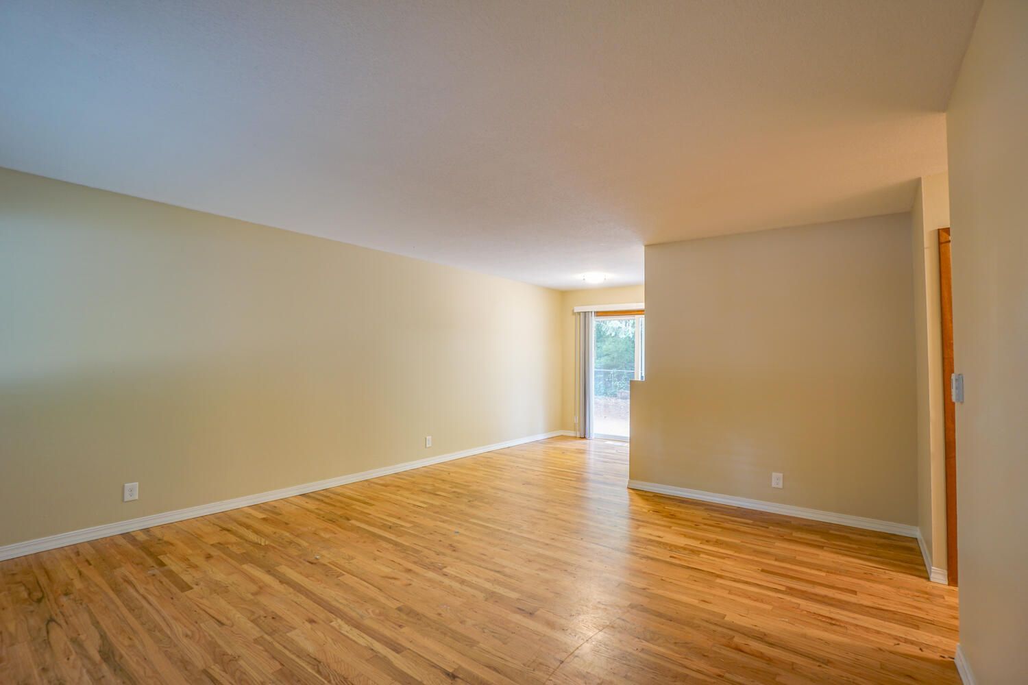 An empty living room with hardwood floors and beige walls.
