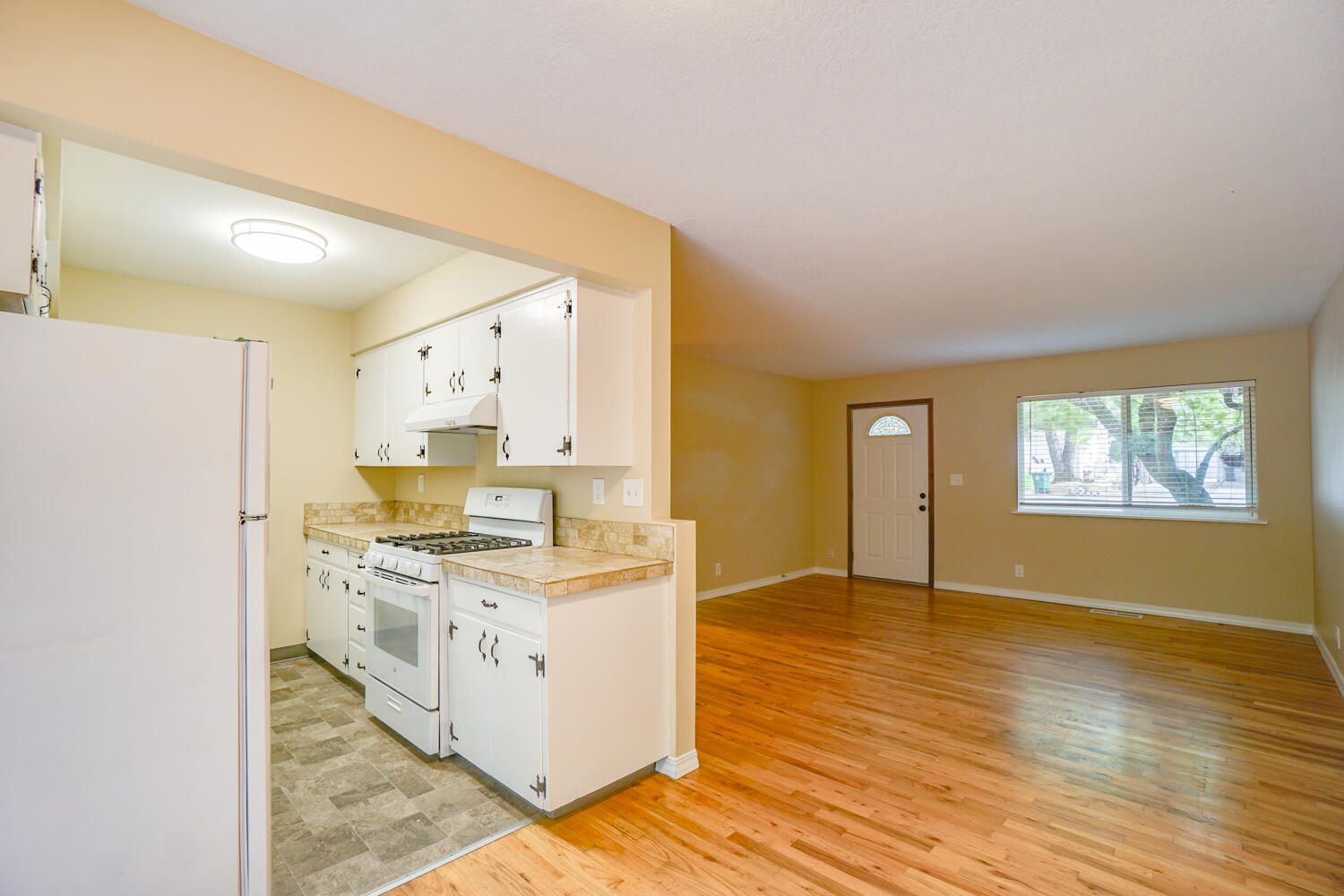 A kitchen with white cabinets , a refrigerator , a stove , and a window.