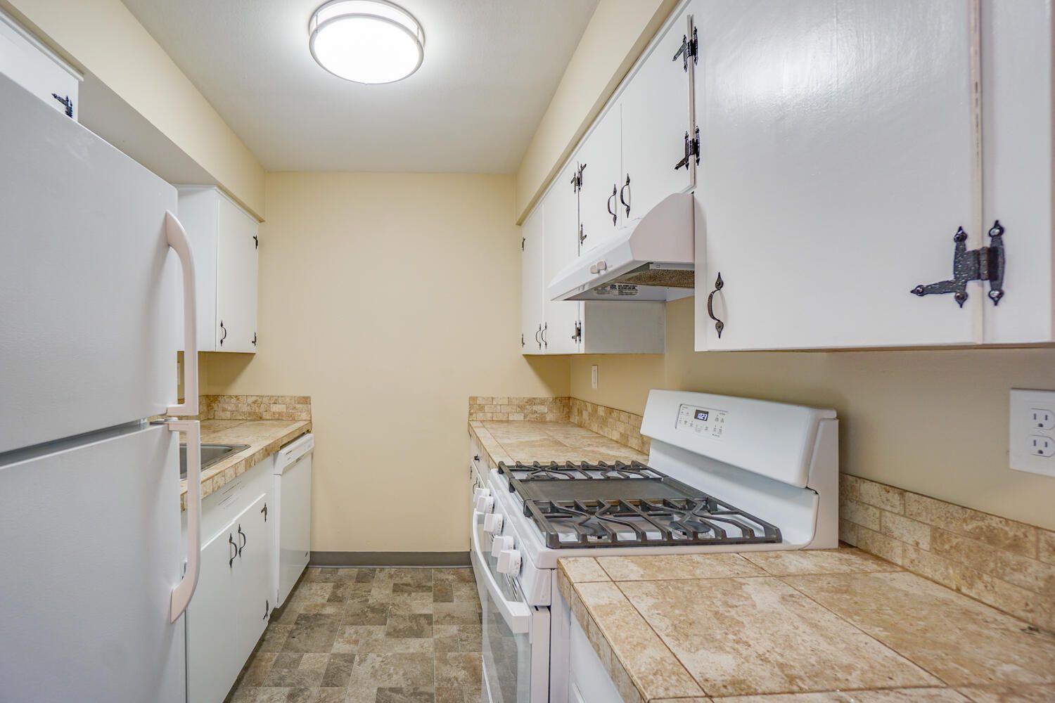 A kitchen with white cabinets , a stove , a refrigerator , and a sink.