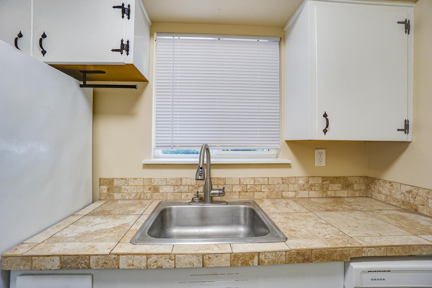 A kitchen with a stainless steel sink and white cabinets.